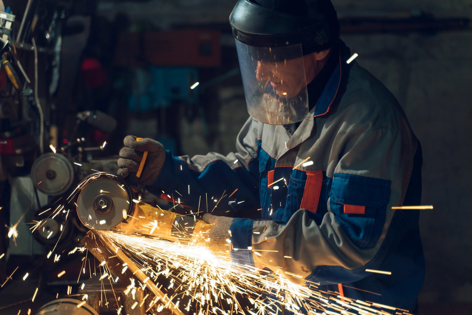 A man using an abrasive wheel tool while wearing proper PPE including gloves, jacket, and face shield.