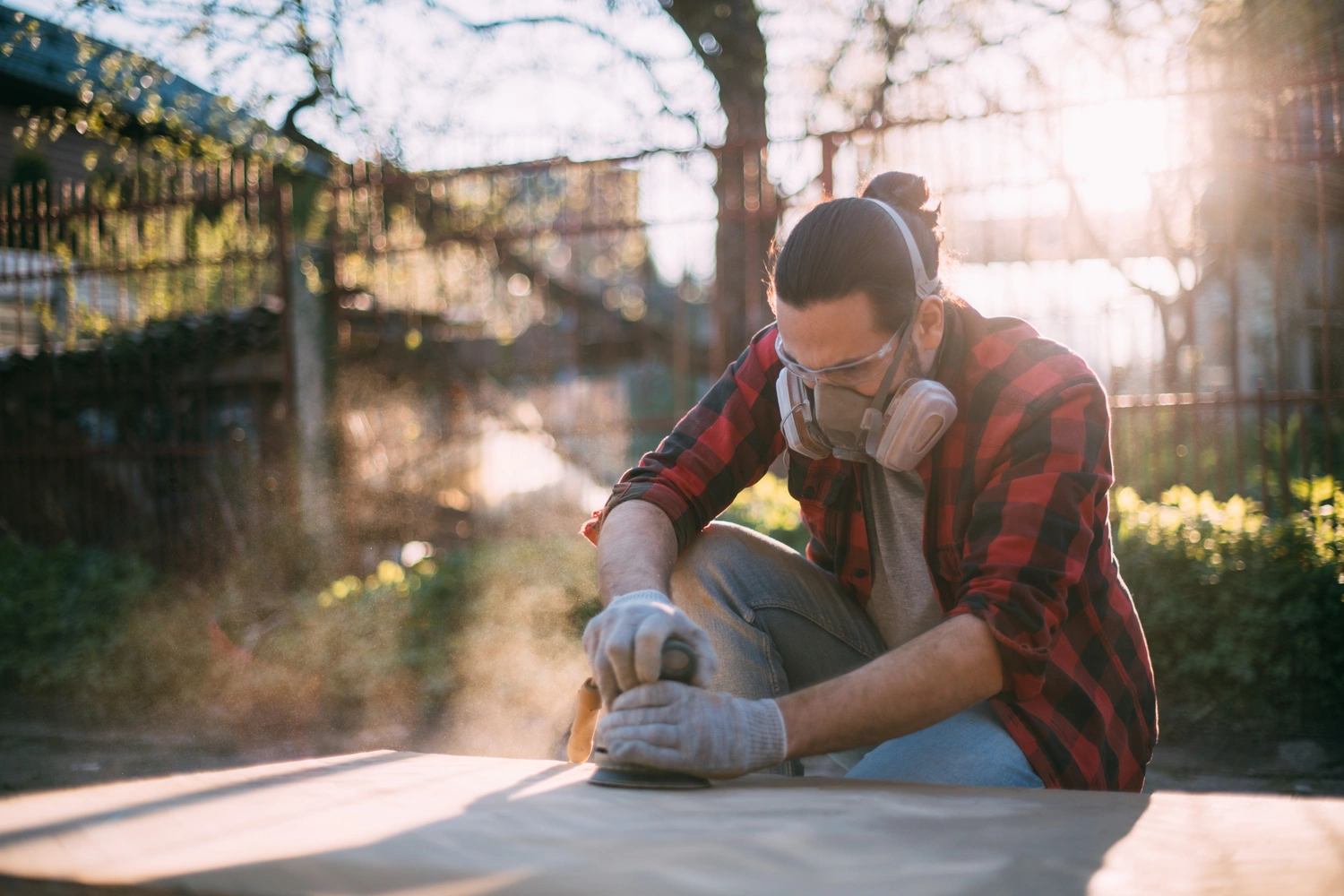 A man using a sander while wearing gloves, respirator, and safety glasses.